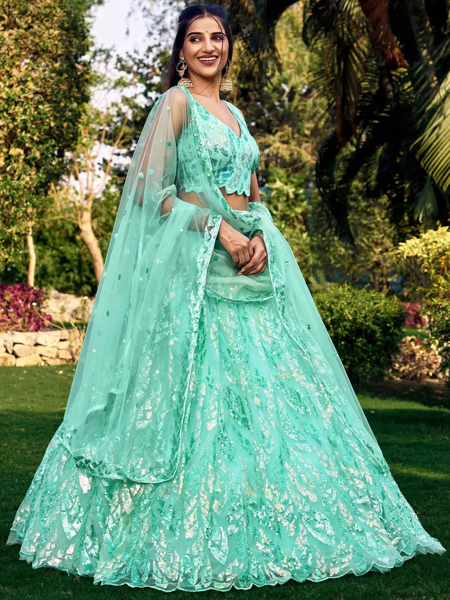 Woman in a light blue traditional outfit standing outdoors with greenery in the background